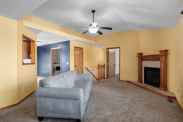 living room featuring washer / clothes dryer, ceiling fan, a tile fireplace, and light carpet