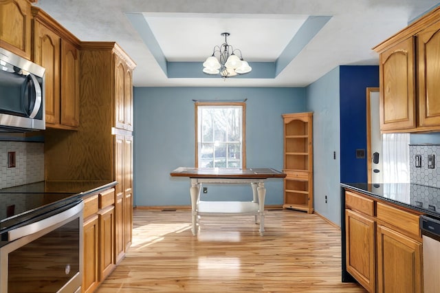 kitchen featuring backsplash, a tray ceiling, stainless steel appliances, decorative light fixtures, and a chandelier