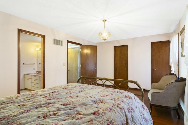 bedroom featuring two closets, visible vents, ensuite bath, and wood finished floors