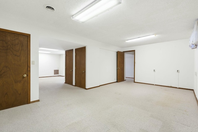 finished below grade area with light carpet, visible vents, a textured ceiling, and baseboards