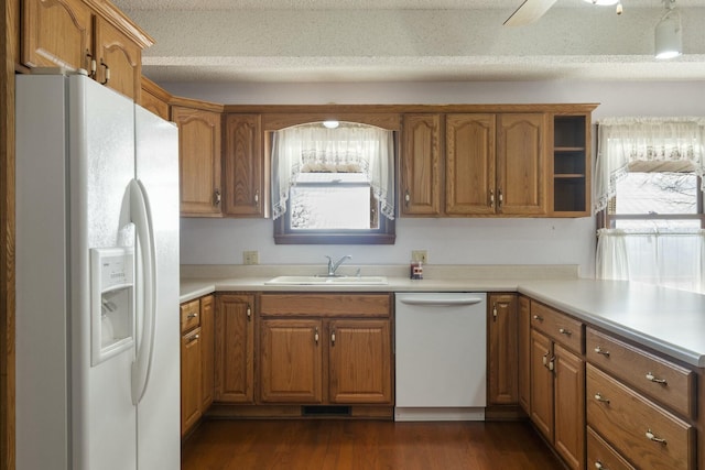 kitchen with a sink, white appliances, dark wood-style floors, and brown cabinetry