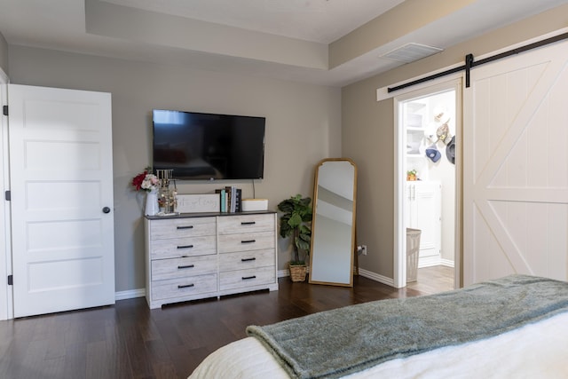 bedroom with a barn door, dark hardwood / wood-style flooring, and ensuite bath