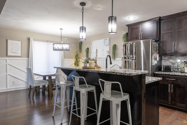 kitchen with a kitchen breakfast bar, dark wood-type flooring, decorative light fixtures, a center island, and stainless steel refrigerator