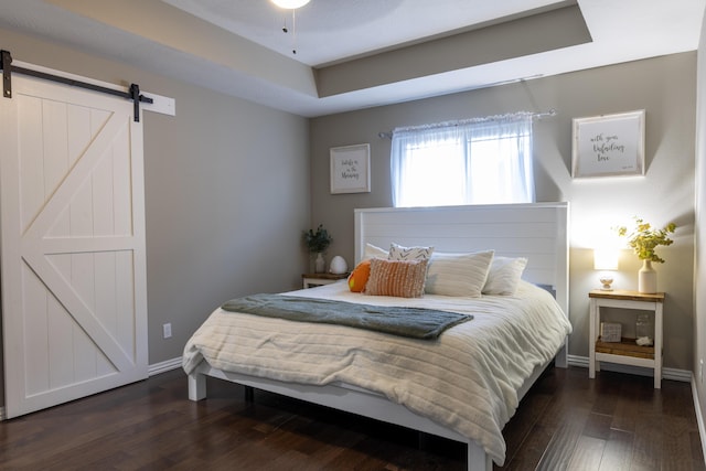 bedroom featuring ceiling fan, a barn door, and dark wood-type flooring