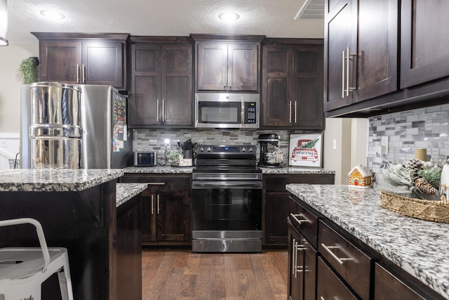 kitchen with light stone counters, dark wood-type flooring, appliances with stainless steel finishes, and tasteful backsplash