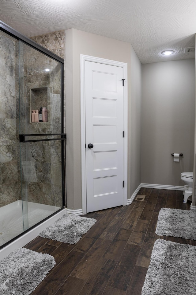 bathroom featuring toilet, wood-type flooring, and a shower with door