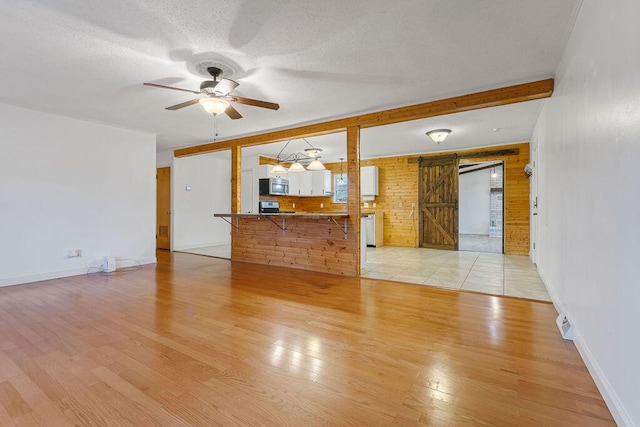 unfurnished living room featuring beam ceiling, a barn door, light wood-type flooring, and a textured ceiling