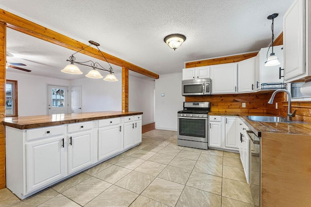 kitchen with sink, hanging light fixtures, kitchen peninsula, white cabinets, and appliances with stainless steel finishes