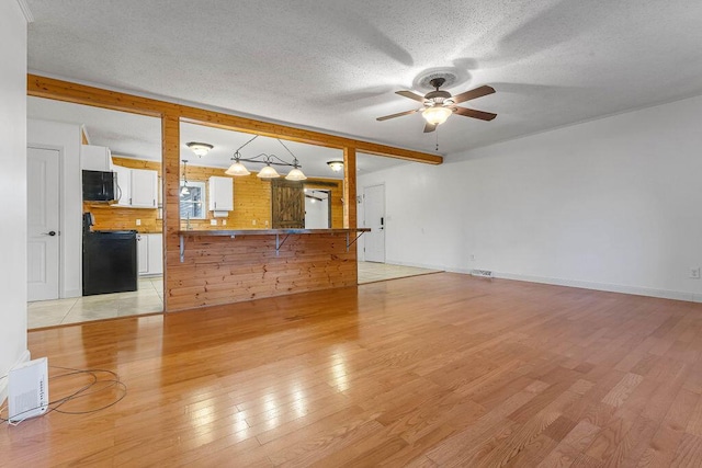 unfurnished living room with beamed ceiling, ceiling fan, light hardwood / wood-style floors, and a textured ceiling