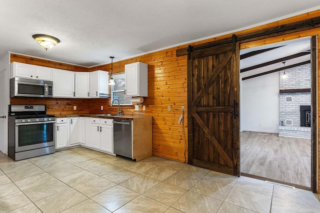 kitchen featuring appliances with stainless steel finishes, sink, a barn door, white cabinets, and hanging light fixtures