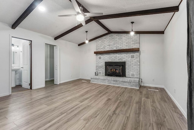 unfurnished living room with a textured ceiling, ceiling fan, lofted ceiling with beams, light hardwood / wood-style flooring, and a fireplace