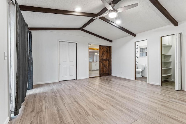 unfurnished bedroom featuring lofted ceiling with beams, connected bathroom, light hardwood / wood-style floors, and ceiling fan