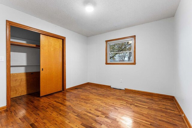 unfurnished bedroom with wood-type flooring, a textured ceiling, and a closet