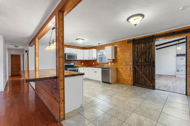 kitchen with stainless steel appliances, pendant lighting, a barn door, white cabinets, and light hardwood / wood-style floors