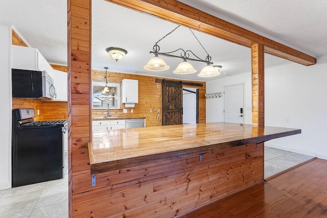 kitchen featuring appliances with stainless steel finishes, light wood-type flooring, pendant lighting, a barn door, and white cabinetry