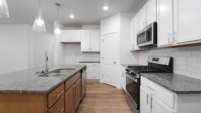 kitchen with appliances with stainless steel finishes, sink, white cabinetry, hanging light fixtures, and an island with sink