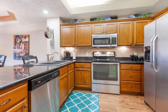 kitchen featuring sink, light hardwood / wood-style floors, a textured ceiling, decorative backsplash, and appliances with stainless steel finishes