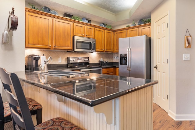 kitchen featuring light wood-type flooring, appliances with stainless steel finishes, tasteful backsplash, a kitchen bar, and kitchen peninsula