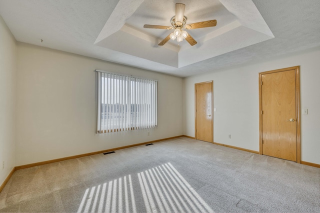 carpeted empty room featuring a tray ceiling, ceiling fan, and a textured ceiling