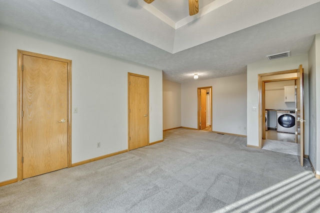 unfurnished bedroom with ceiling fan, washer / dryer, light colored carpet, and a textured ceiling