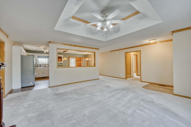 unfurnished living room with ceiling fan with notable chandelier, light colored carpet, crown molding, and a tray ceiling