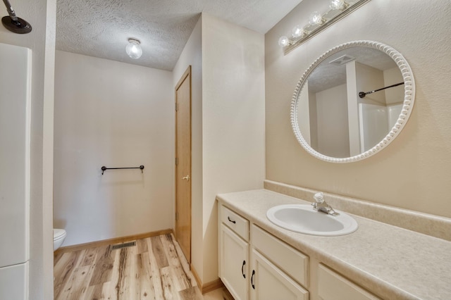 bathroom with wood-type flooring, vanity, a textured ceiling, and toilet