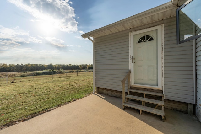 entrance to property featuring a lawn, a patio area, and a rural view