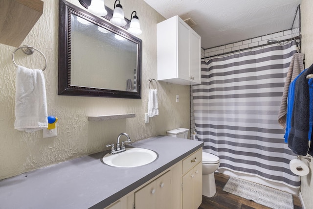 bathroom with walk in shower, vanity, a textured ceiling, wood-type flooring, and toilet