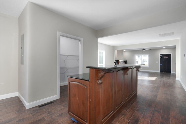 kitchen featuring a breakfast bar, dark wood-type flooring, electric panel, ceiling fan, and a kitchen island