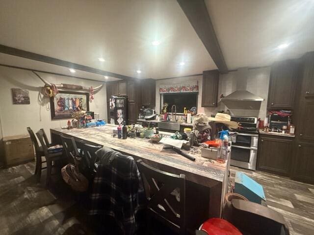 kitchen featuring wall chimney range hood, sink, a breakfast bar area, dark brown cabinets, and range with two ovens