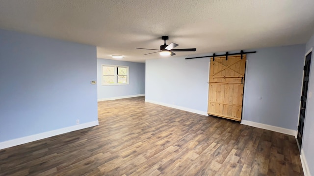 empty room with dark hardwood / wood-style floors, a barn door, a textured ceiling, and ceiling fan