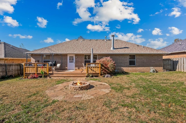 back of property with a deck, an outdoor fire pit, and a yard