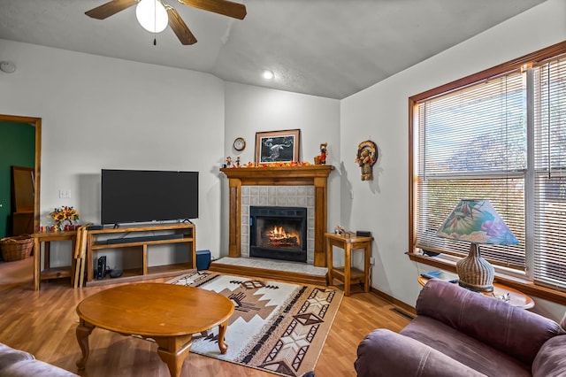 living room featuring ceiling fan, light hardwood / wood-style floors, a fireplace, and vaulted ceiling