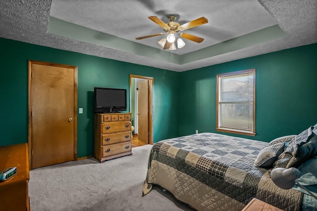 carpeted bedroom featuring a textured ceiling, a tray ceiling, and ceiling fan