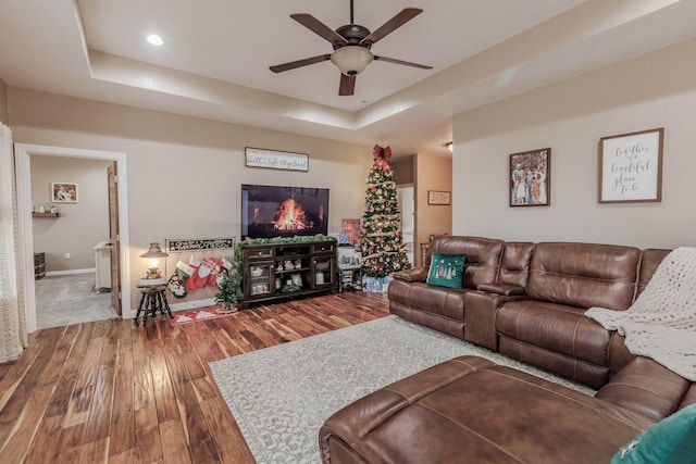 living area featuring a tray ceiling, ceiling fan, baseboards, and wood finished floors