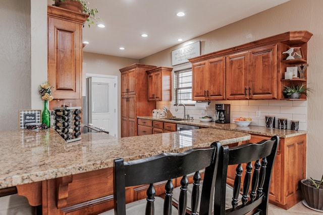 kitchen featuring brown cabinets, tasteful backsplash, a sink, a peninsula, and a kitchen bar