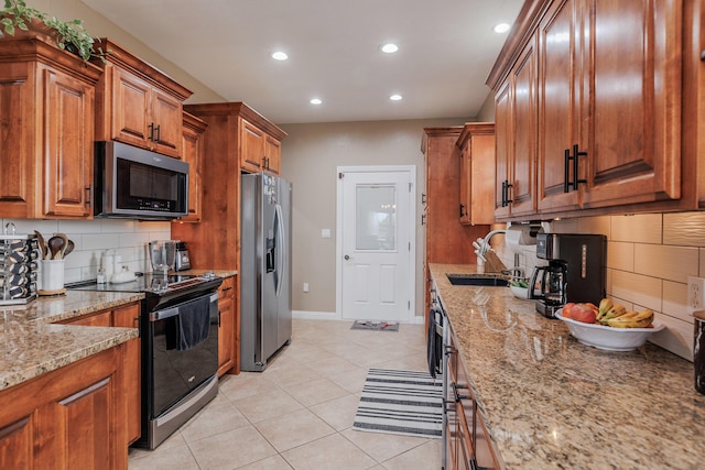 kitchen featuring light tile patterned floors, light stone counters, stainless steel appliances, a sink, and brown cabinets