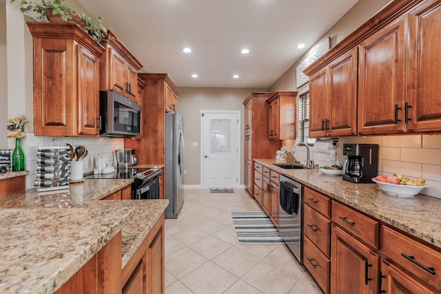 kitchen featuring light tile patterned floors, stainless steel appliances, a sink, brown cabinets, and light stone countertops