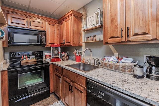 kitchen with light stone counters, brown cabinetry, a sink, a drop ceiling, and black appliances