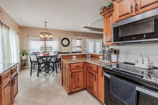 kitchen featuring light tile patterned floors, brown cabinets, a peninsula, a tray ceiling, and stainless steel appliances