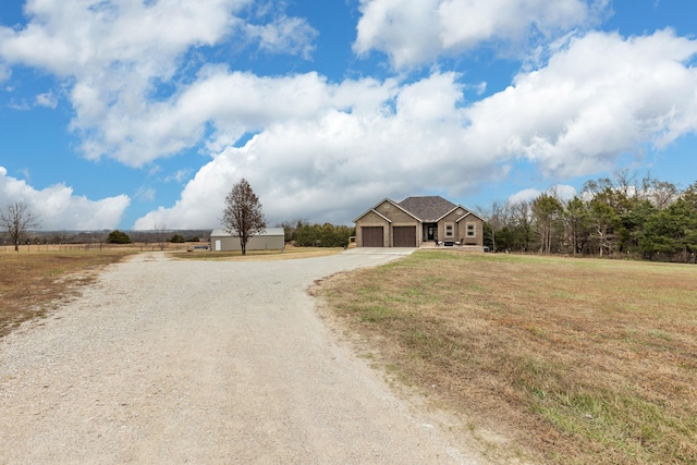 view of front of property featuring dirt driveway, a rural view, a front yard, and a garage