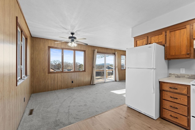 kitchen with light hardwood / wood-style floors, a textured ceiling, ceiling fan, white fridge, and wood walls