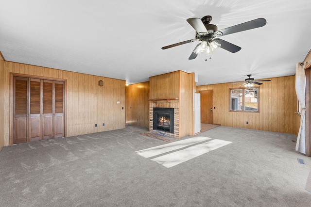 unfurnished living room featuring a fireplace, light carpet, ceiling fan, and wooden walls