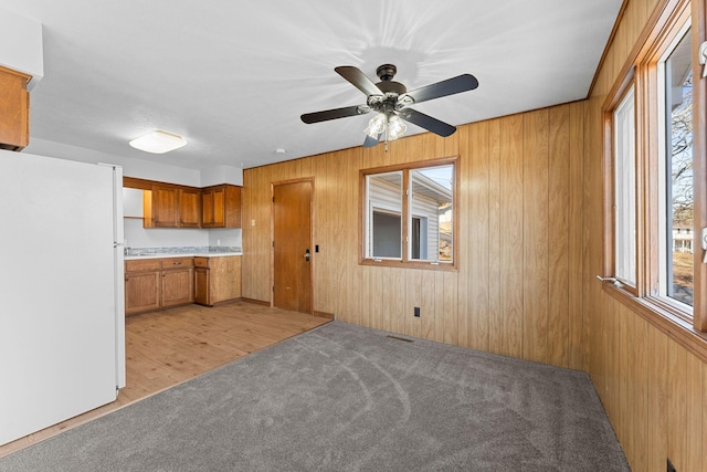 kitchen featuring wood walls, ceiling fan, white fridge, and light hardwood / wood-style floors