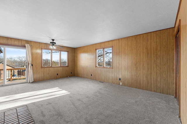 unfurnished living room with carpet flooring, a textured ceiling, ceiling fan, and wooden walls