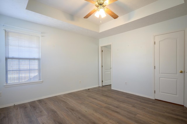 unfurnished room featuring a tray ceiling, dark hardwood / wood-style floors, and ceiling fan