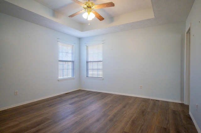 spare room featuring a raised ceiling, ceiling fan, and dark wood-type flooring