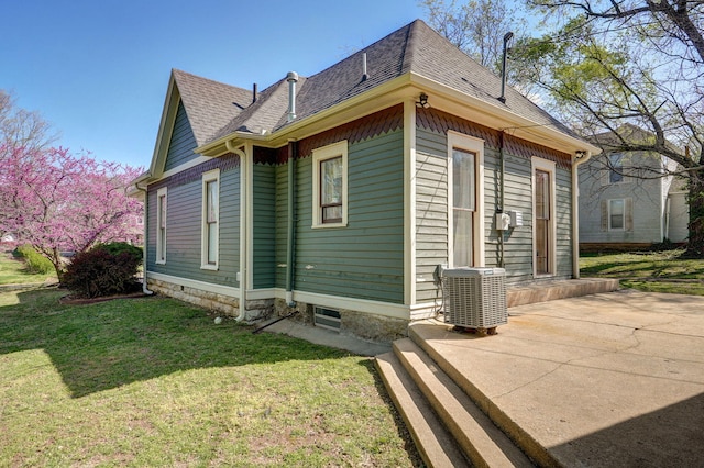 view of side of home with central AC, a shingled roof, and a lawn