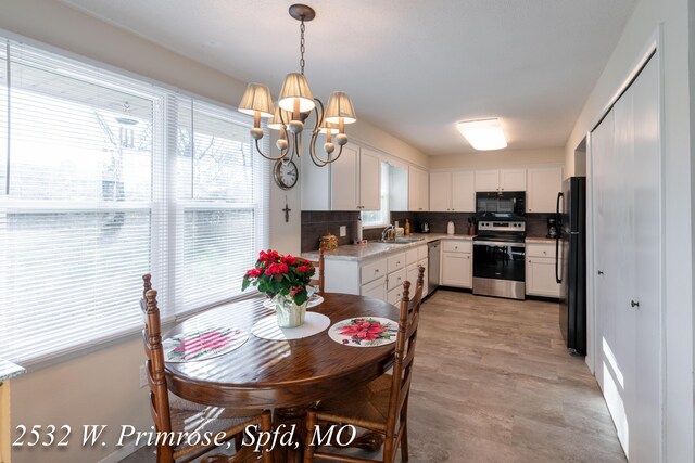 kitchen featuring backsplash, black appliances, sink, hanging light fixtures, and white cabinetry