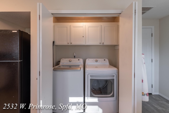 laundry area featuring washing machine and clothes dryer, dark wood-type flooring, and cabinets